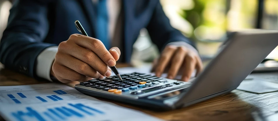 Businessman using a calculator with laptop and financial documents.